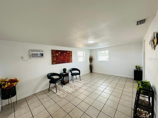 living area with a textured ceiling, light tile patterned floors, and a wall mounted air conditioner