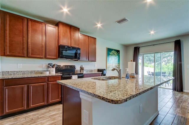 kitchen with an island with sink, sink, light stone countertops, black appliances, and light hardwood / wood-style floors