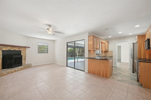 kitchen featuring light tile patterned floors, stainless steel appliances, sink, a stone fireplace, and ceiling fan