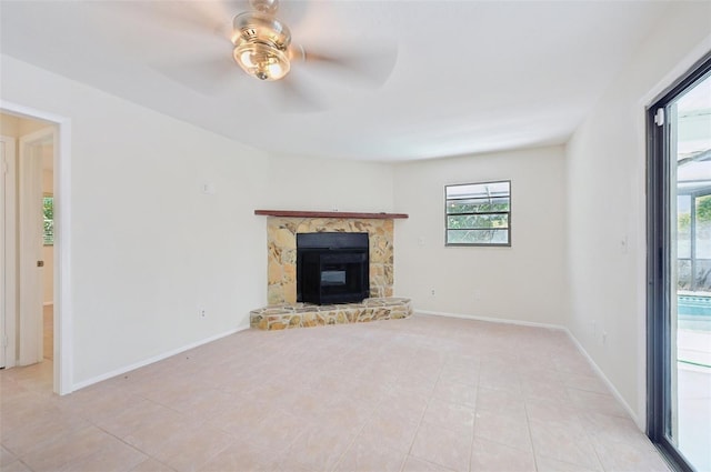 unfurnished living room featuring a healthy amount of sunlight, light tile patterned flooring, ceiling fan, and a stone fireplace