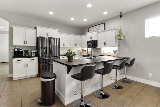 kitchen featuring white cabinets, sink, light tile patterned floors, a kitchen bar, and stainless steel fridge with ice dispenser