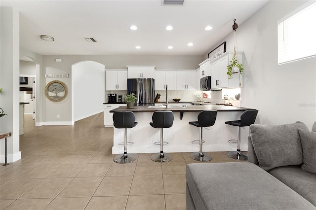 kitchen featuring tasteful backsplash, stainless steel fridge with ice dispenser, white cabinetry, a breakfast bar area, and light tile patterned flooring