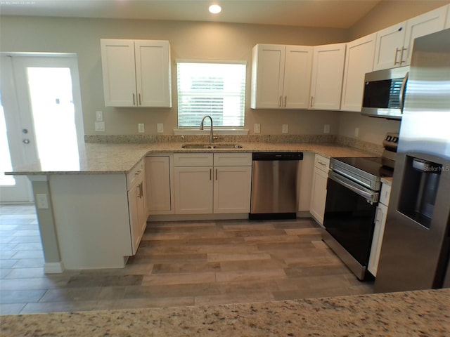 kitchen featuring appliances with stainless steel finishes, light stone countertops, white cabinetry, sink, and kitchen peninsula