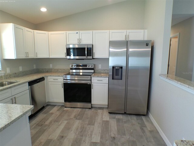 kitchen featuring vaulted ceiling, appliances with stainless steel finishes, white cabinets, and light hardwood / wood-style floors