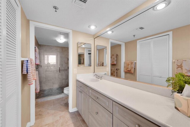 bathroom with a textured ceiling, vanity, a tile shower, toilet, and tile patterned floors