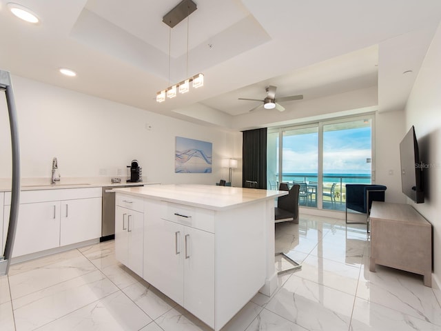 kitchen featuring ceiling fan, a center island, a raised ceiling, and white cabinetry