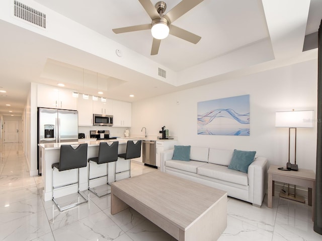 living room featuring ceiling fan, a raised ceiling, and sink