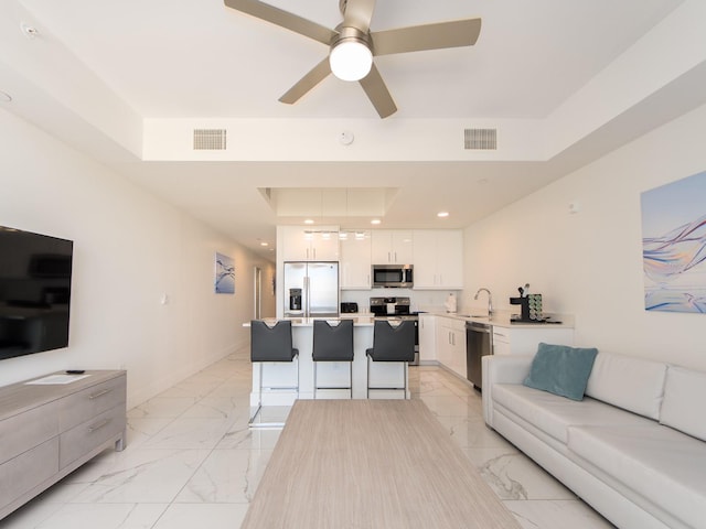 living room featuring ceiling fan, sink, and a tray ceiling