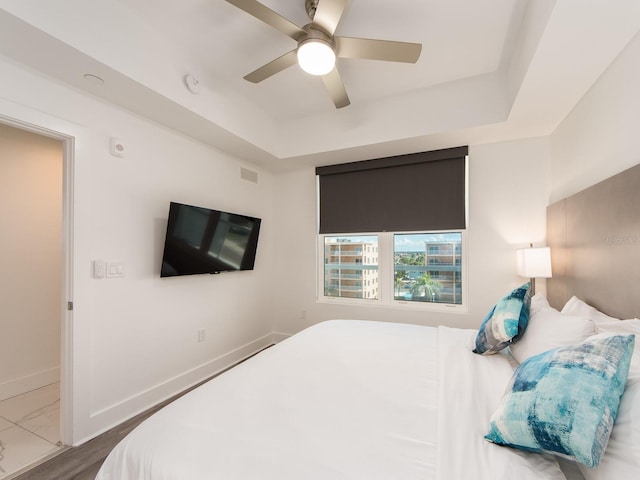 bedroom featuring ceiling fan, a tray ceiling, and dark hardwood / wood-style flooring