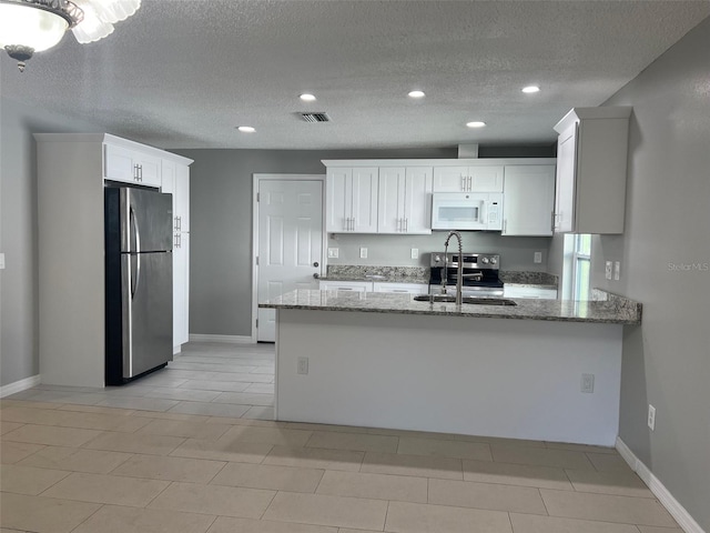 kitchen with a textured ceiling, kitchen peninsula, light stone countertops, appliances with stainless steel finishes, and white cabinets