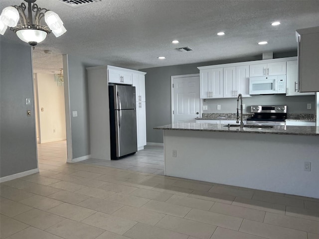 kitchen with a textured ceiling, a notable chandelier, stainless steel appliances, dark stone countertops, and white cabinets