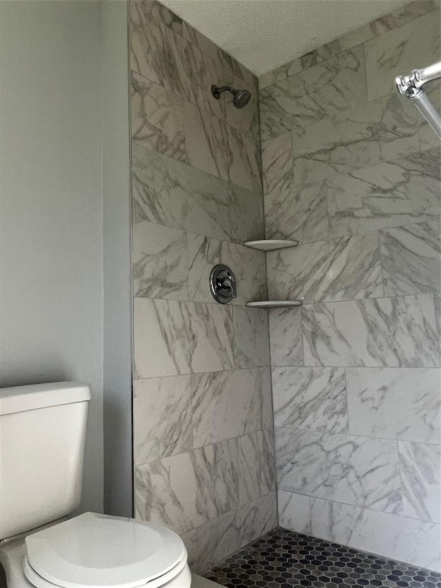 bathroom featuring a textured ceiling, toilet, and a tile shower