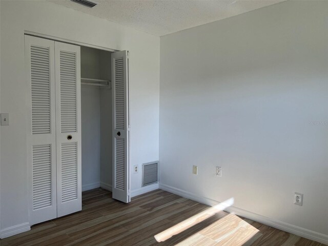 unfurnished bedroom featuring dark wood-type flooring, a closet, and a textured ceiling