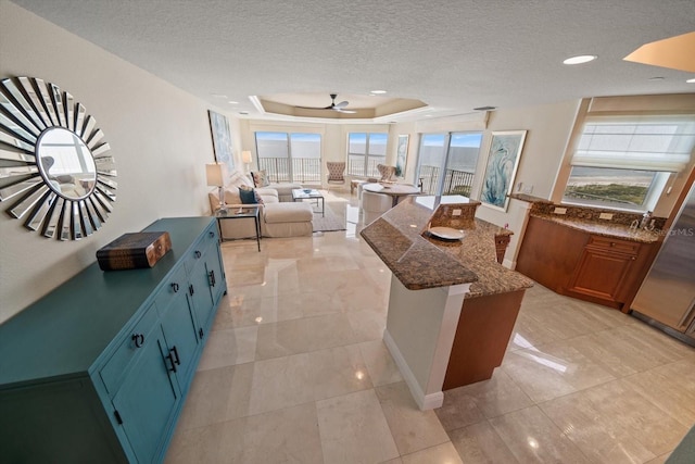 kitchen with a textured ceiling, a kitchen island, blue cabinetry, dark stone counters, and a raised ceiling