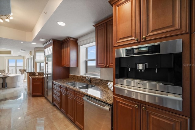 kitchen featuring stainless steel appliances, dark stone countertops, a sink, and brown cabinets