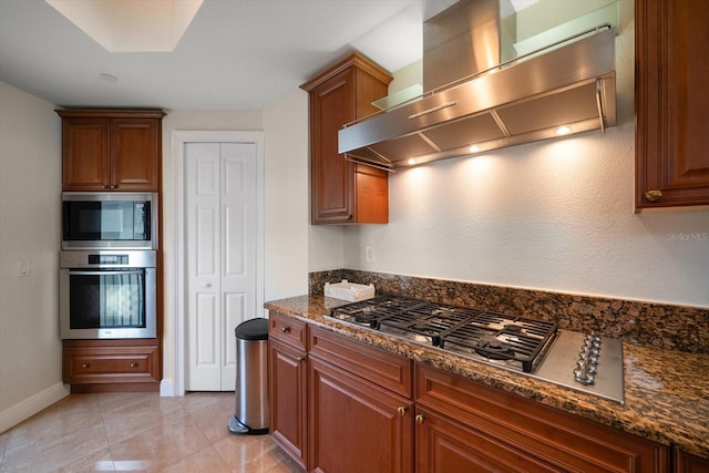 kitchen with light tile patterned floors, brown cabinetry, appliances with stainless steel finishes, dark stone countertops, and extractor fan