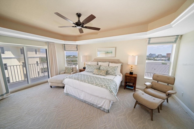 carpeted bedroom with access to exterior, a raised ceiling, multiple windows, and baseboards