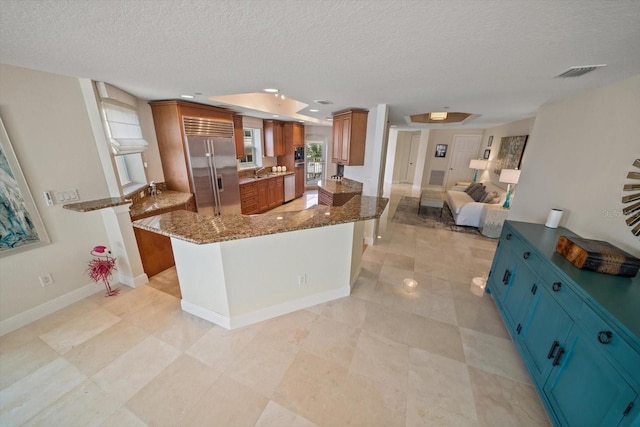 kitchen with brown cabinets, open floor plan, stainless steel built in fridge, and visible vents