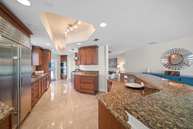 kitchen with built in appliances, brown cabinetry, a raised ceiling, and a textured ceiling