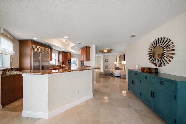 kitchen with a textured ceiling, recessed lighting, visible vents, stainless steel built in fridge, and dark stone countertops