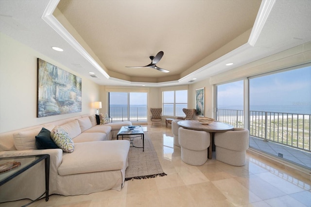 living area with a ceiling fan, a tray ceiling, and a water view