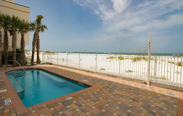 community pool featuring a patio area, fence, a view of the beach, and a water view