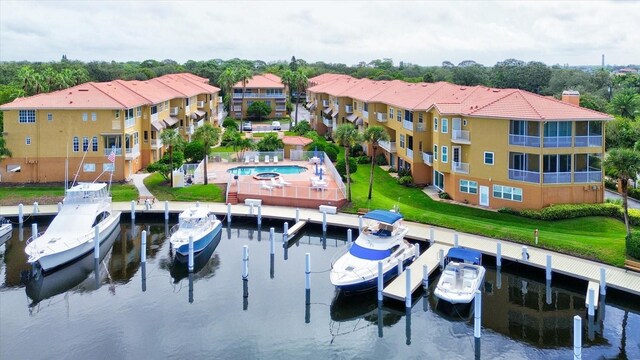 view of dock with a community pool, a water view, a lawn, and a balcony