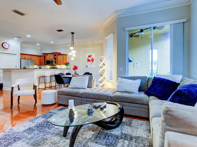 living room featuring crown molding, light hardwood / wood-style flooring, and ceiling fan with notable chandelier