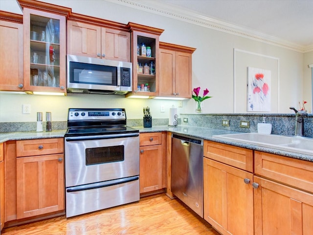 kitchen featuring stone counters, light hardwood / wood-style flooring, stainless steel appliances, sink, and ornamental molding