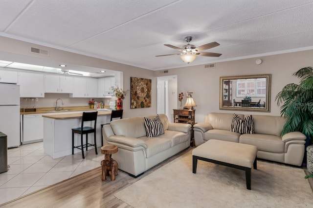 tiled living room with a textured ceiling, ceiling fan, ornamental molding, and sink