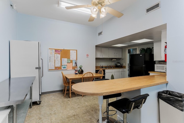 kitchen featuring visible vents, a sink, freestanding refrigerator, a peninsula, and white microwave