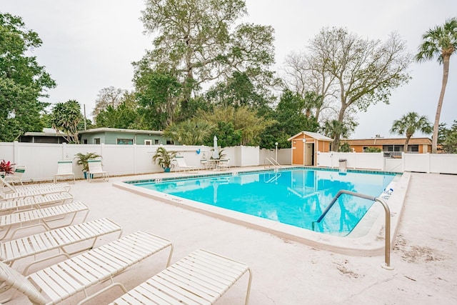 community pool with an outdoor structure, a storage unit, a patio area, and a fenced backyard