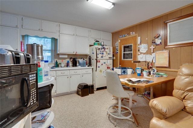 kitchen with a textured ceiling, wood walls, white refrigerator, and white cabinets