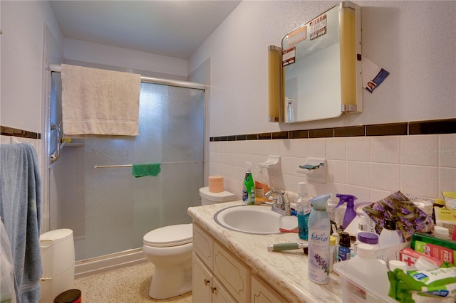 bathroom with a shower with door, vanity, backsplash, tile walls, and toilet