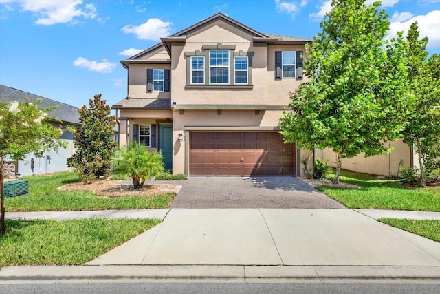 view of front of house featuring stucco siding, decorative driveway, a garage, and a front lawn