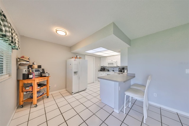 kitchen with white appliances, a kitchen bar, kitchen peninsula, sink, and white cabinets