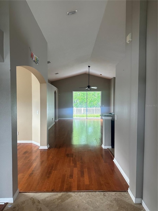 empty room with arched walkways, wood finished floors, visible vents, baseboards, and vaulted ceiling