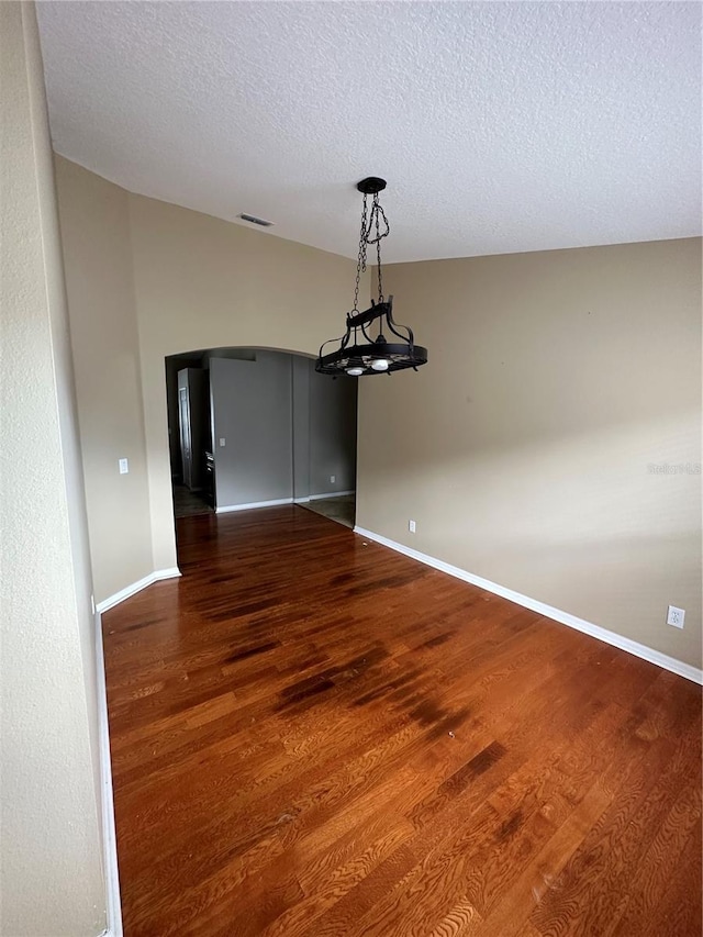 unfurnished dining area featuring arched walkways, a textured ceiling, wood finished floors, visible vents, and baseboards