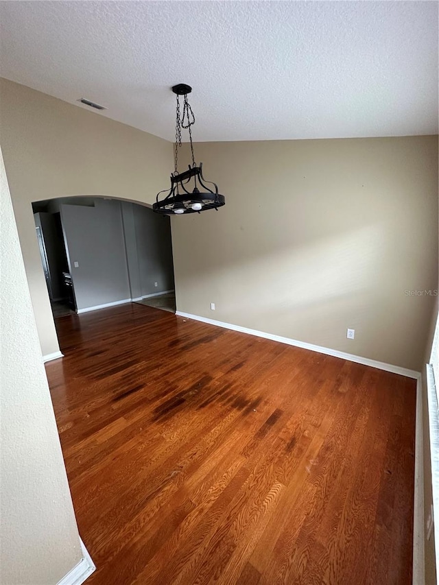 unfurnished dining area with baseboards, a textured ceiling, arched walkways, and wood finished floors