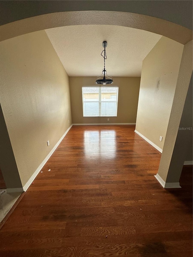 unfurnished dining area featuring baseboards, a textured ceiling, arched walkways, and wood finished floors