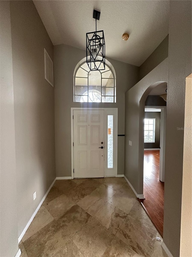 foyer entrance with arched walkways, visible vents, a towering ceiling, a textured ceiling, and baseboards