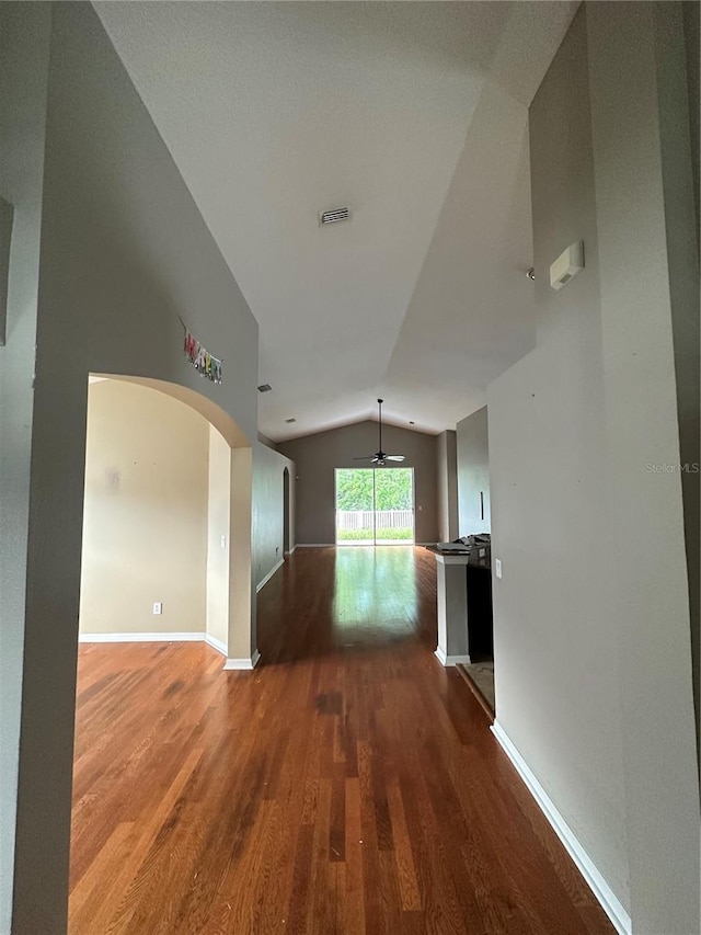 hall featuring arched walkways, lofted ceiling, visible vents, wood finished floors, and baseboards