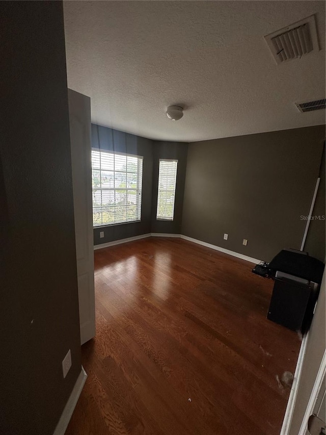 unfurnished room featuring a textured ceiling, wood finished floors, visible vents, and baseboards