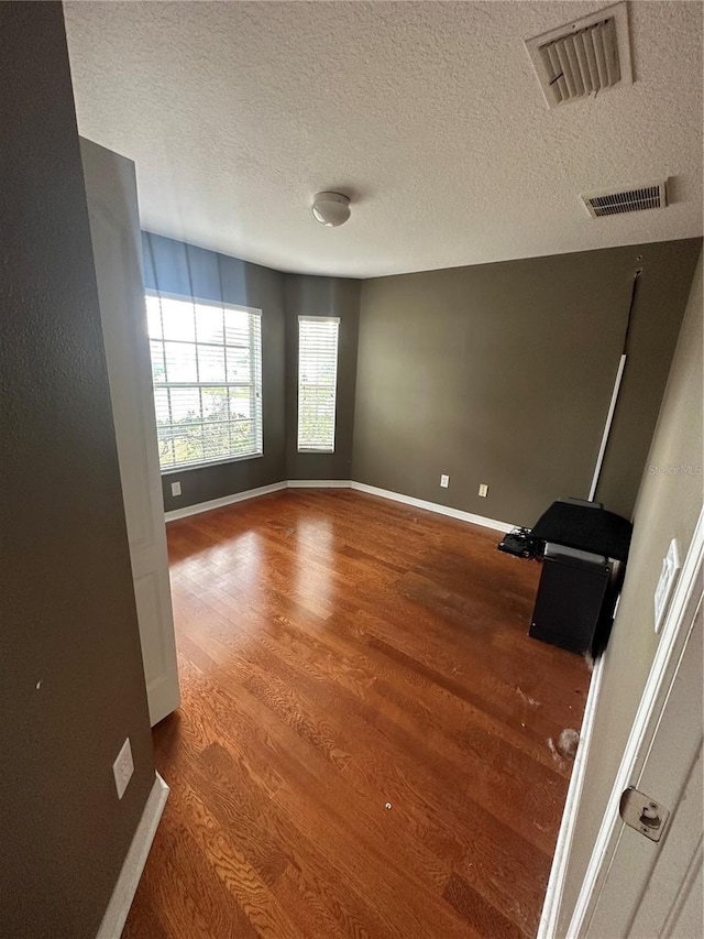 unfurnished room with visible vents, a textured ceiling, baseboards, and wood finished floors