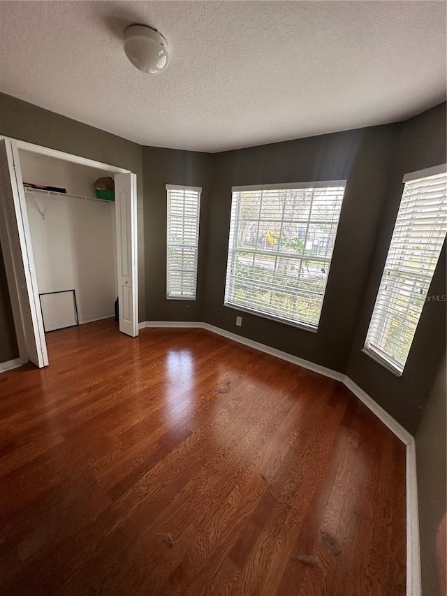 unfurnished bedroom featuring a closet, a textured ceiling, baseboards, and wood finished floors