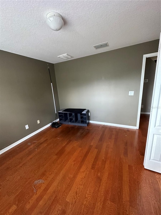 empty room featuring baseboards, a textured ceiling, visible vents, and wood finished floors