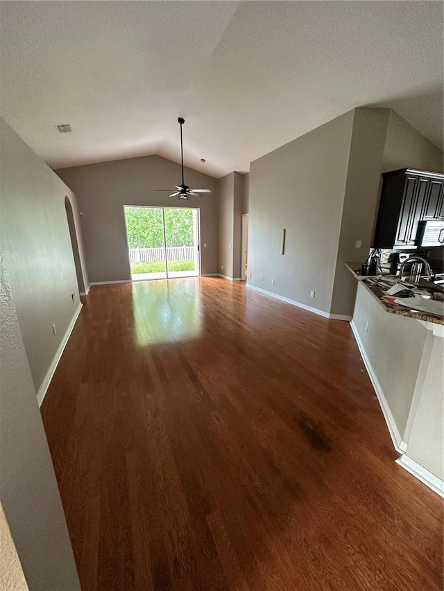 unfurnished living room featuring arched walkways, lofted ceiling, visible vents, wood finished floors, and baseboards