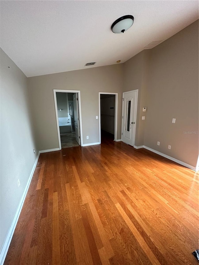 unfurnished bedroom featuring vaulted ceiling, wood finished floors, visible vents, and baseboards