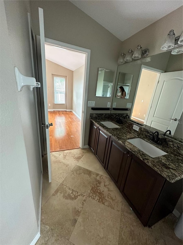 bathroom with vaulted ceiling, double vanity, a sink, and baseboards