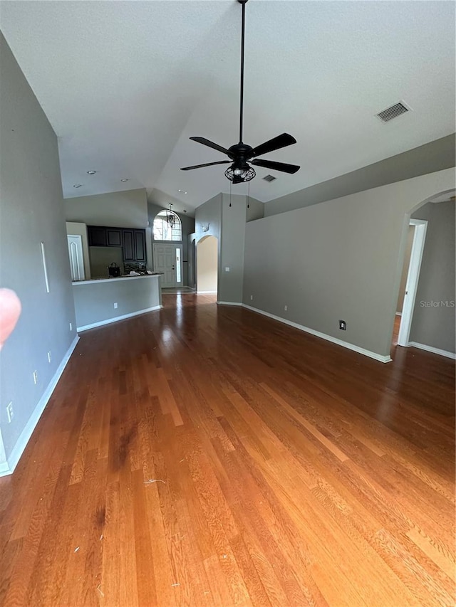 unfurnished living room featuring light wood finished floors, baseboards, arched walkways, a ceiling fan, and vaulted ceiling